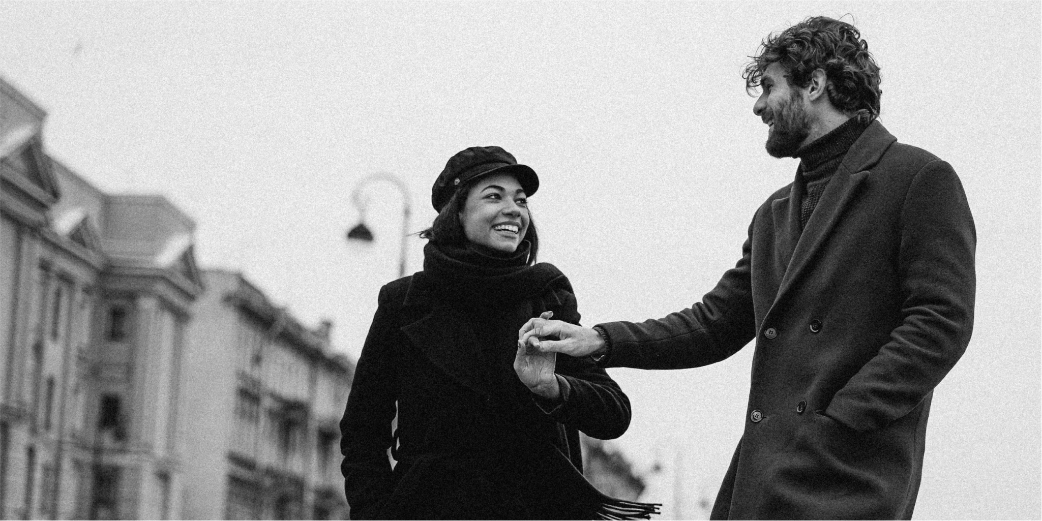 Ein Schwarz-Weiß-Foto eines Mannes und einer Frau, die sich an den Händen halten und die Verbindung zwischen ihnen inmitten natürlicher Elemente einfangen.
